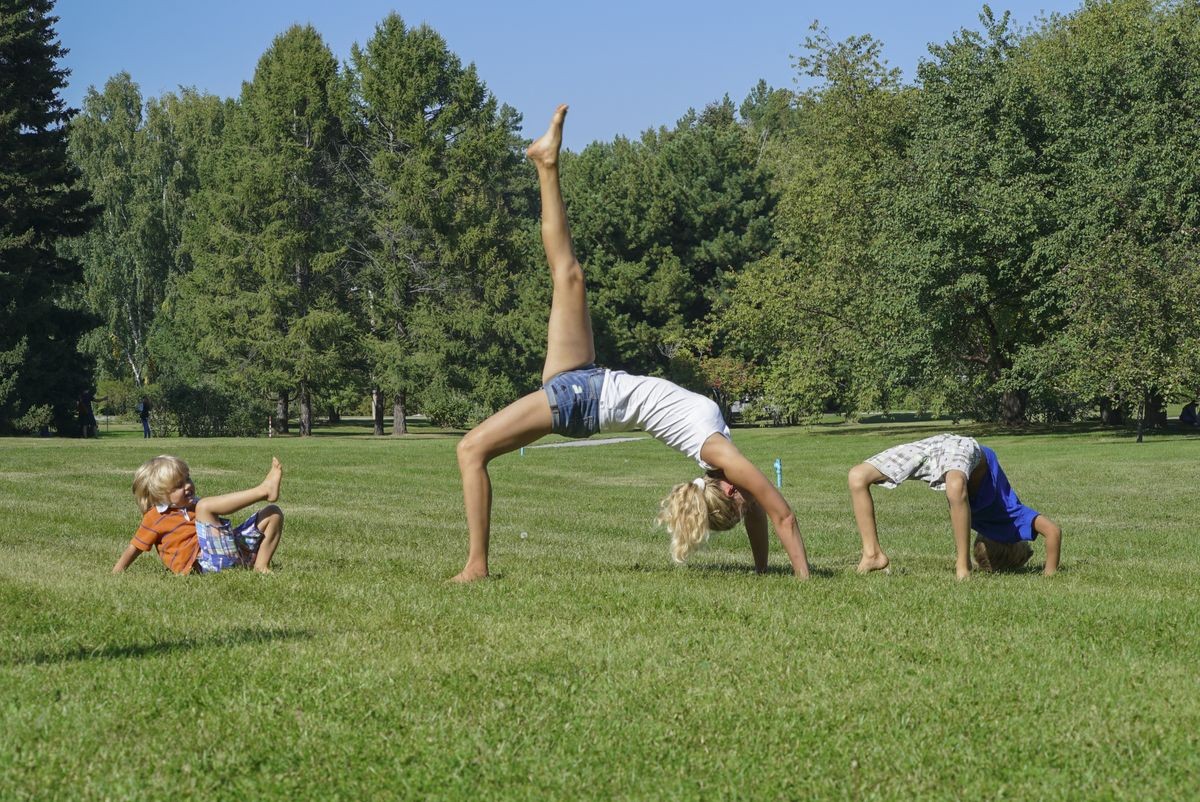 Healthy family practicing yoga in green park. Young woman with children standing in Bridge pose.